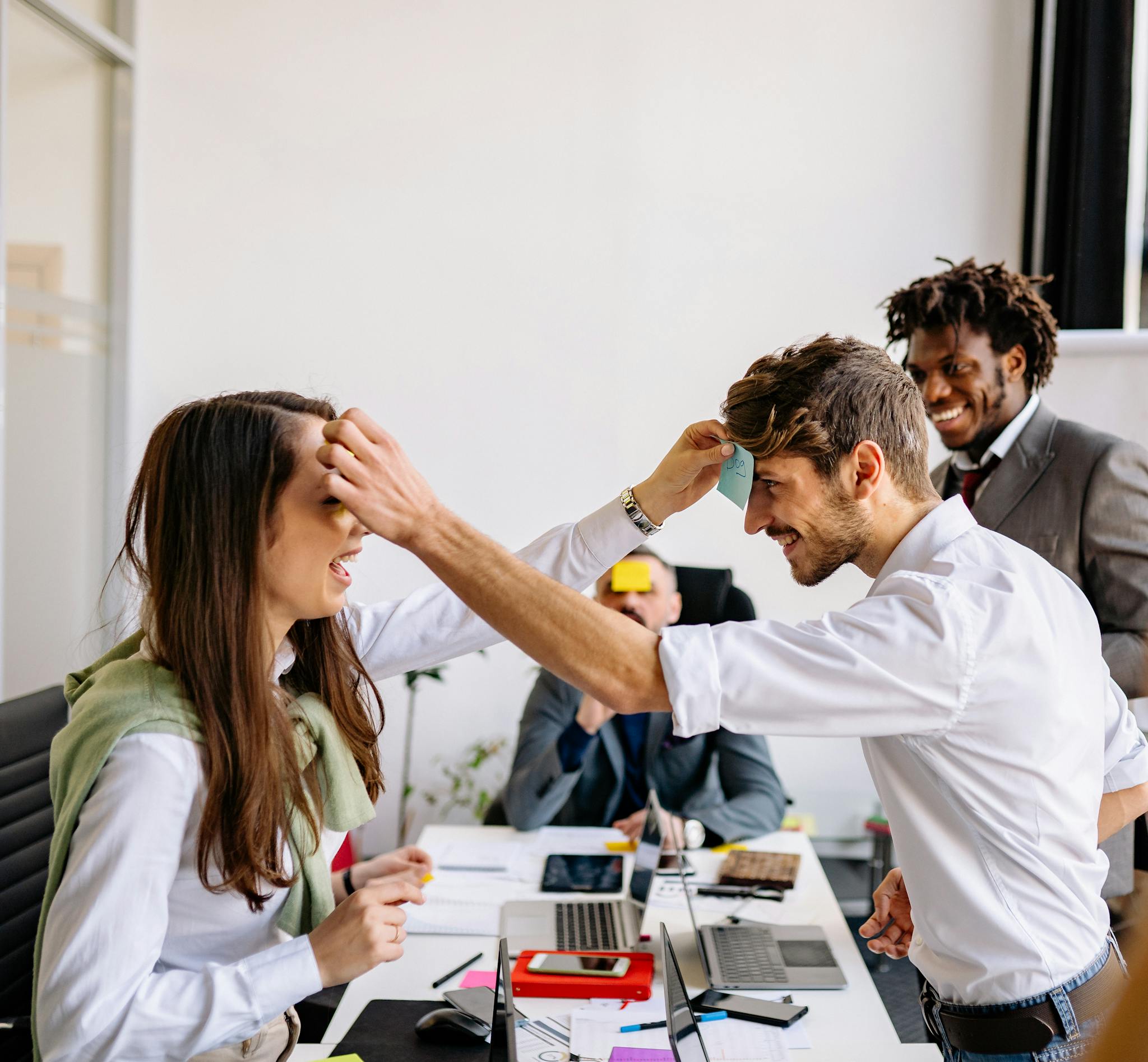 Office colleagues playing a humorous sticky note game during a break, sharing laughter.